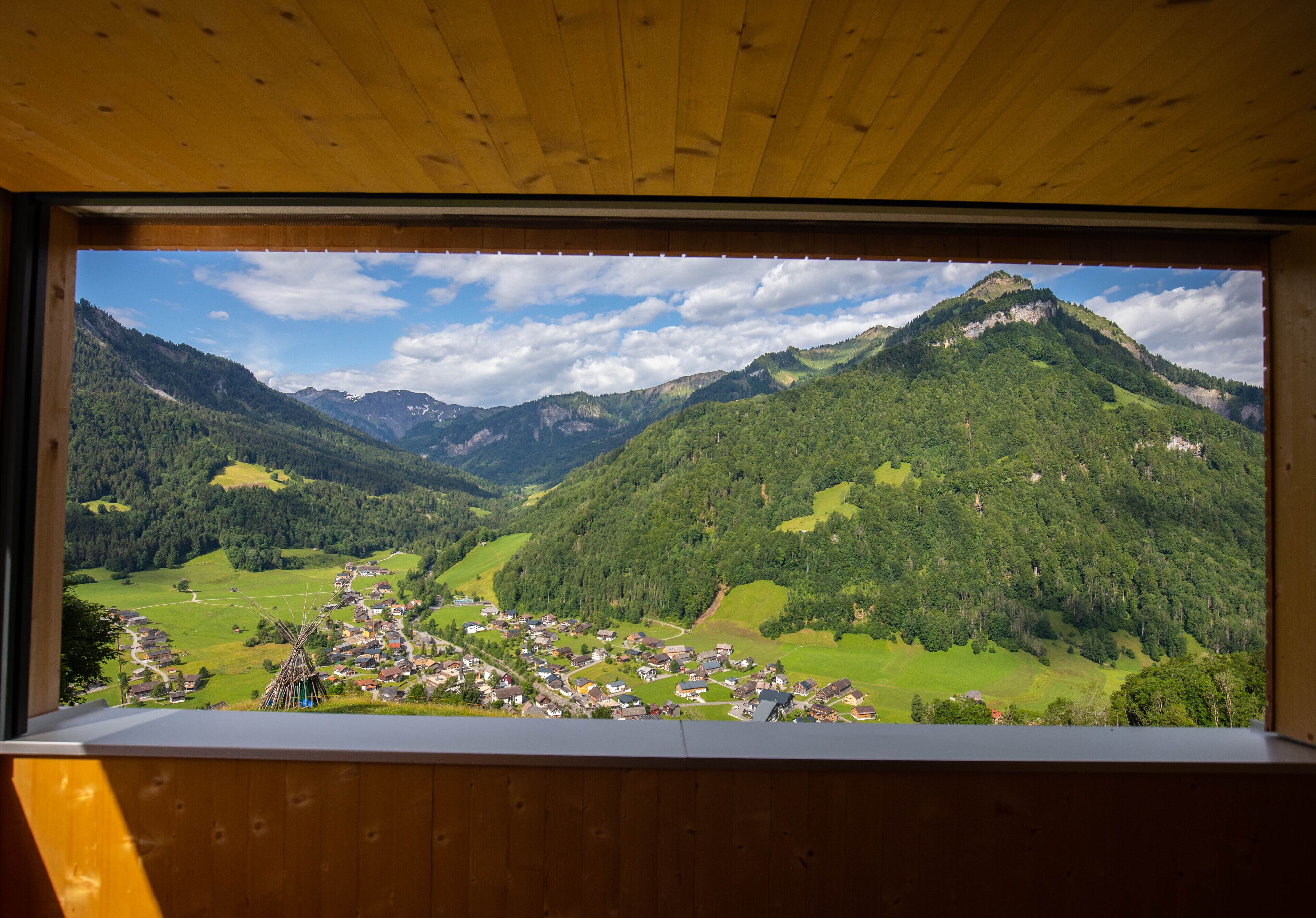 A view from a window overlooking a mountainous landscape with a village below.