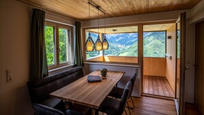 A wooden dining area with a table, benches, and a view of a mountainous landscape through large windows.