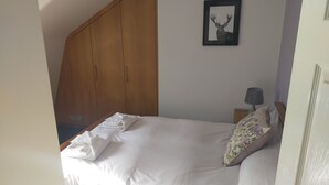 Une chambre à coucher avec un lit, une armoire en bois, un tableau représentant un cerf encadré et une table de chevet avec une lampe.
