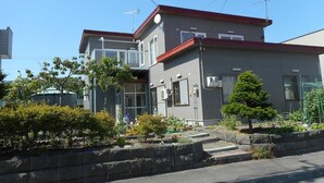A two-story residential building with a red roof, a balcony, and a small garden area with various plants and flowers. - BBQ (千歳市白樺)