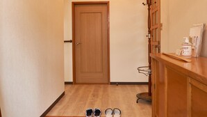 A hallway with a wooden door, a shoe rack with shoes, and a bottle of cleaning gel on a counter. - BBQ (千歳市白樺)