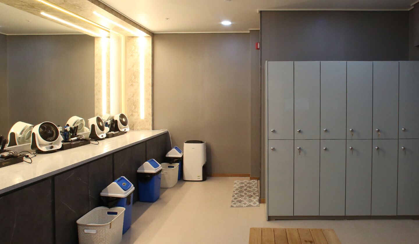 A modern bathroom with a vanity, multiple hair dryers, a trash bin, and a large storage cabinet.