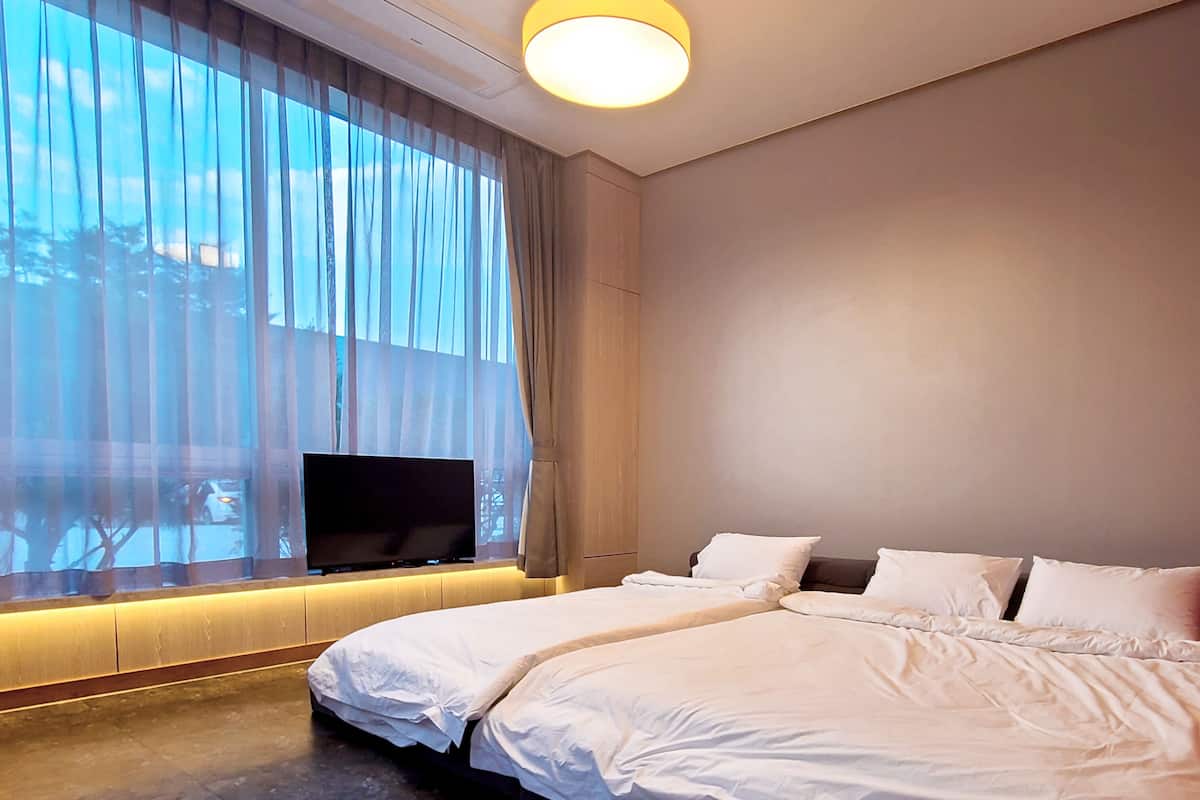 Una habitación de hotel moderna con una cama grande, un televisor de pantalla plana montado en la pared y un ventanal con cortinas traslúcidas.