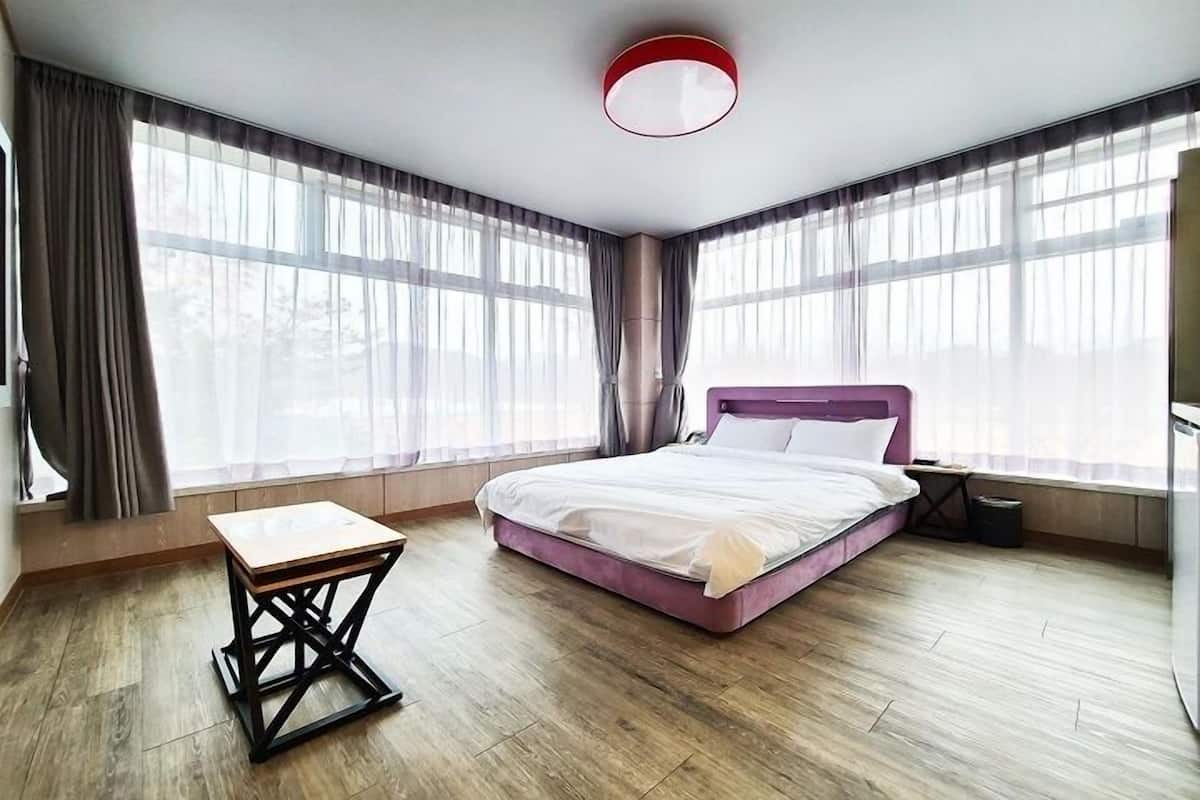 Un dormitorio moderno con una cama, una mesita pequeña y ventanas amplias.