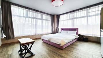 Een moderne slaapkamer met een bed, een klein tafeltje en grote ramen.