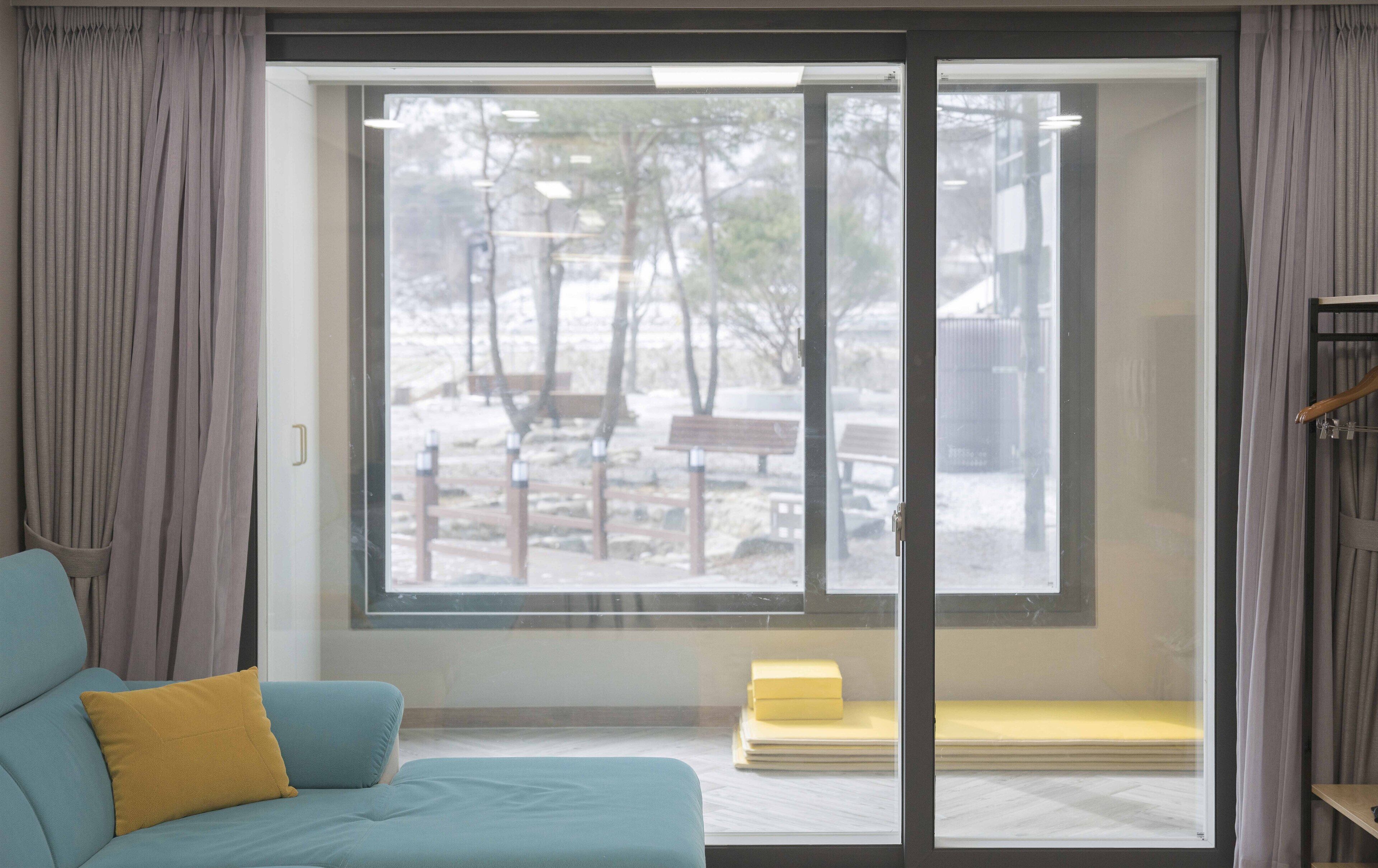 A room with a large window, a sofa with a yellow pillow, and a bench outside.