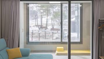 A room with a large window, a sofa with a yellow pillow, and a bench outside.