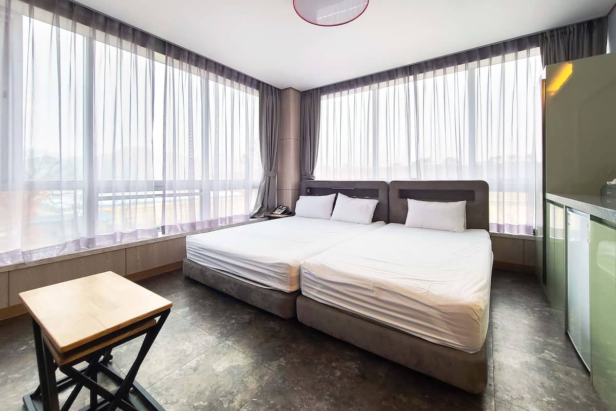 Habitación de hotel con cama doble, una mesita de madera y un ventanal con cortinas translúcidas.