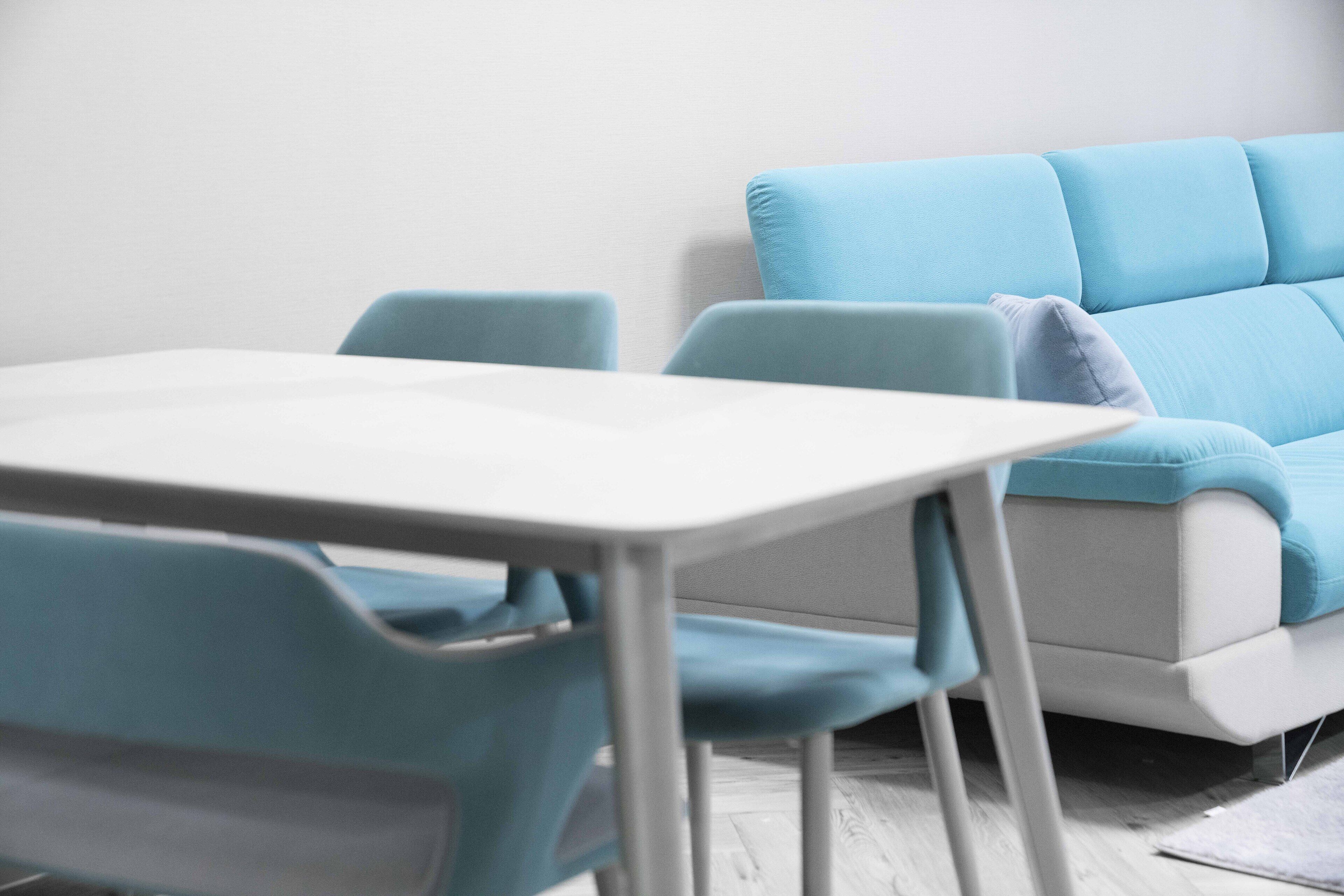 Ein Zimmer mit einem weißen Tisch, blauen Stühlen, einem hellblauen Sofa und einer weißen Wand.