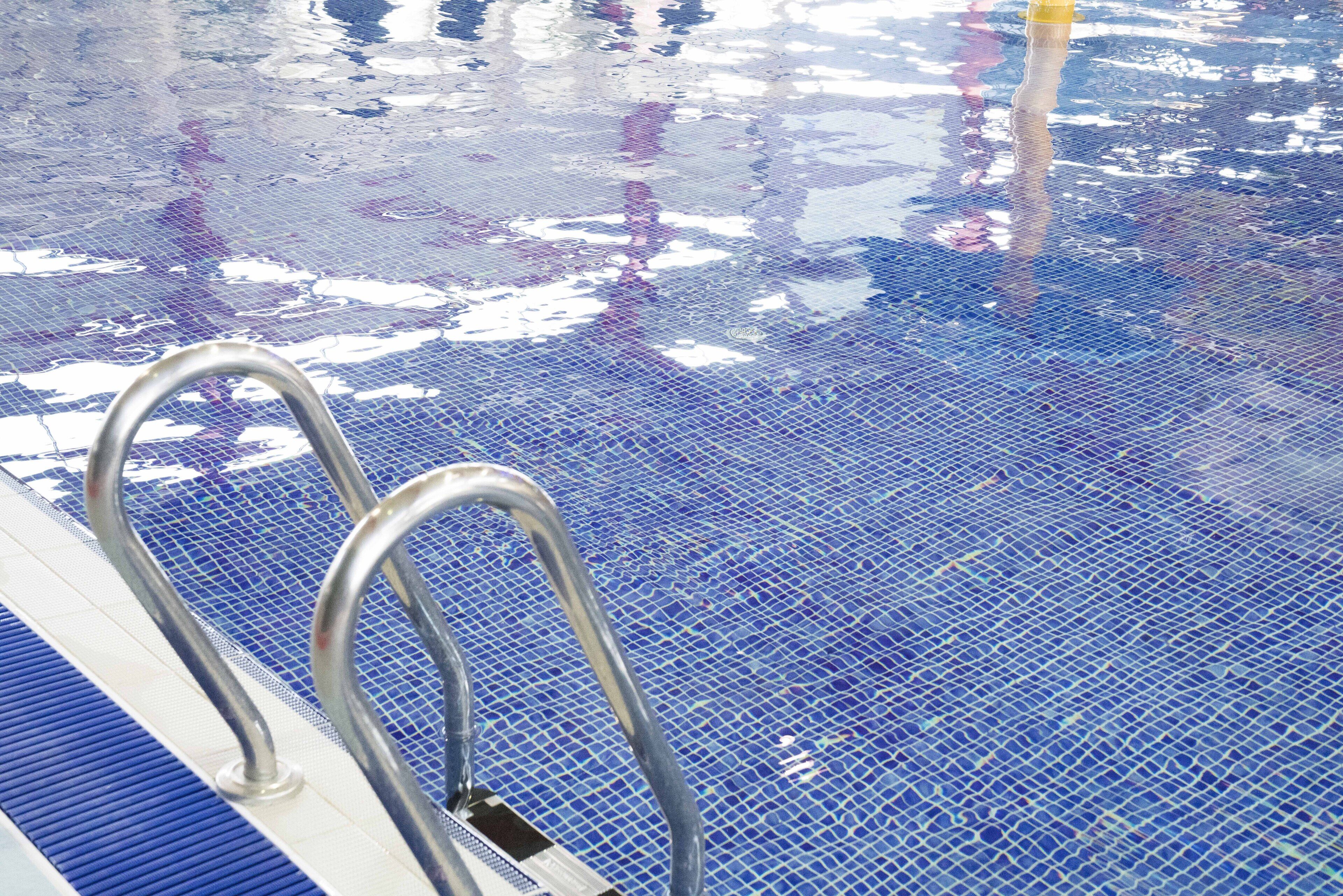 A swimming pool with a blue tiled floor and metal handrails.