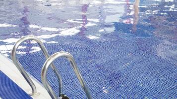 Una piscina con suelo de baldosas azules y barandillas de metal.