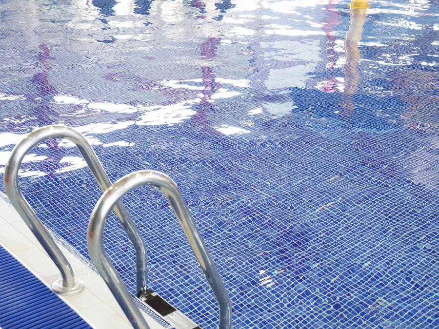 Una piscina con suelo de baldosas azules y barandillas de metal.