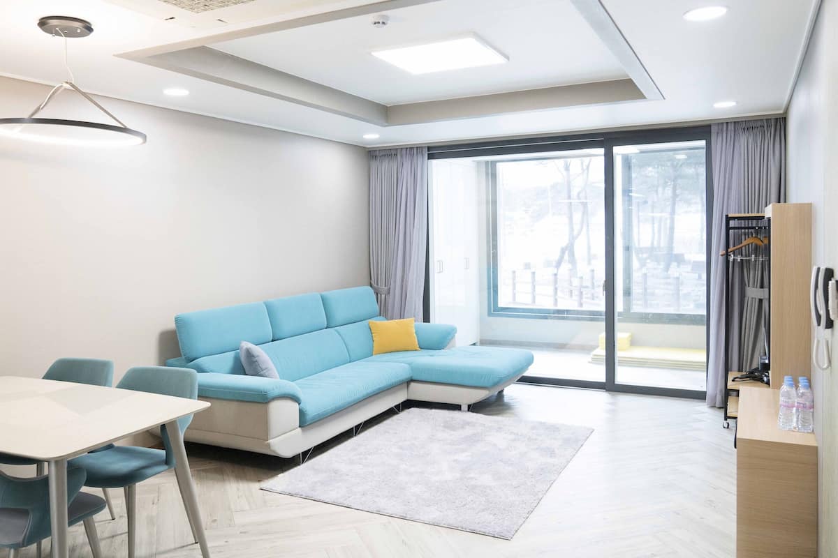 Una sala de estar moderna con un sofá azul, una mesita pequeña y vistas al exterior a través de grandes ventanales.