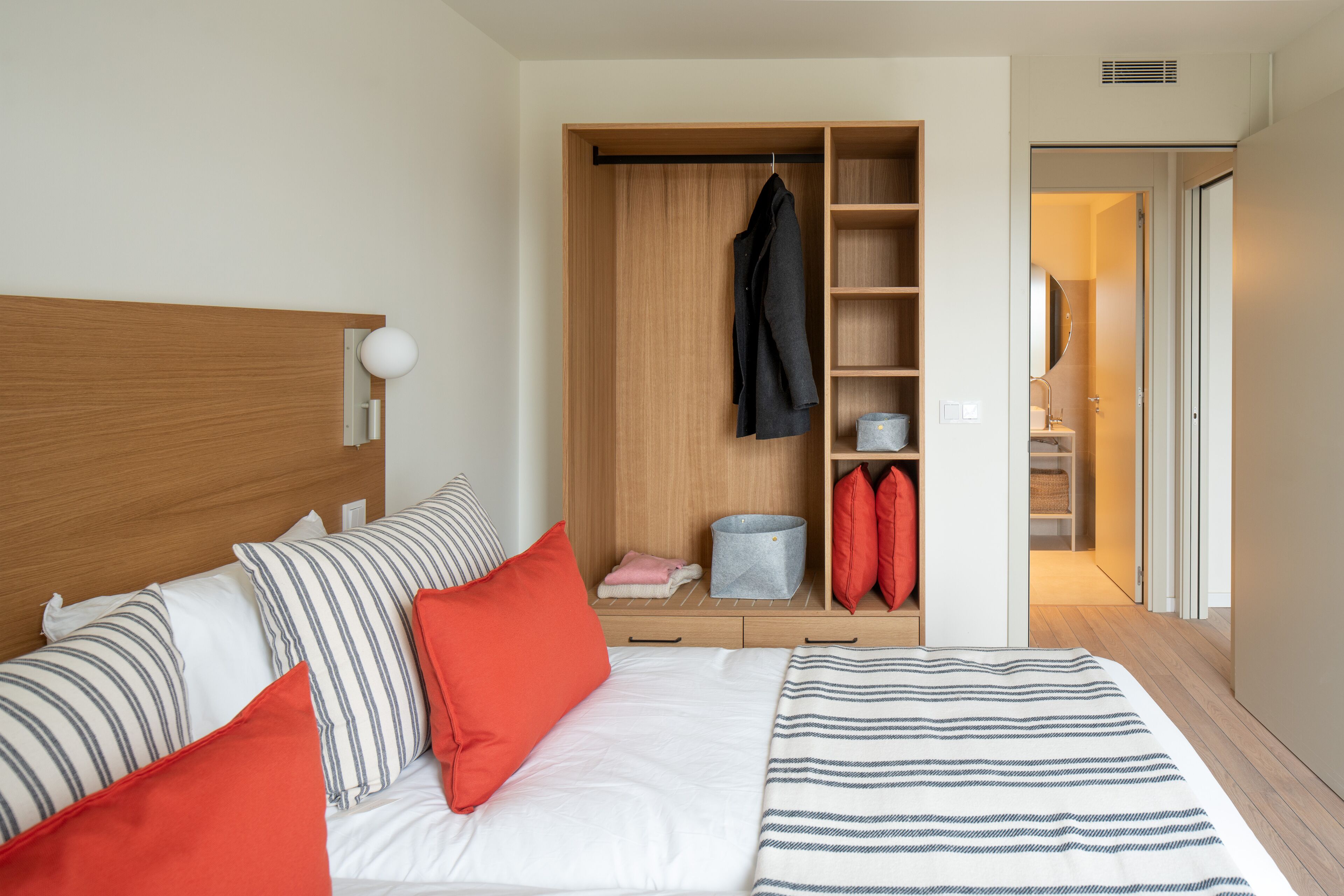Une chambre à coucher bien rangée, avec un lit, des oreillers, une armoire et une salle de bain visible à travers une porte ouverte.