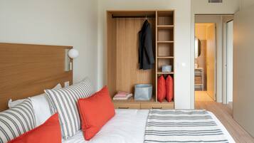 Une chambre à coucher bien rangée, avec un lit, des oreillers, une armoire et une salle de bain visible à travers une porte ouverte.