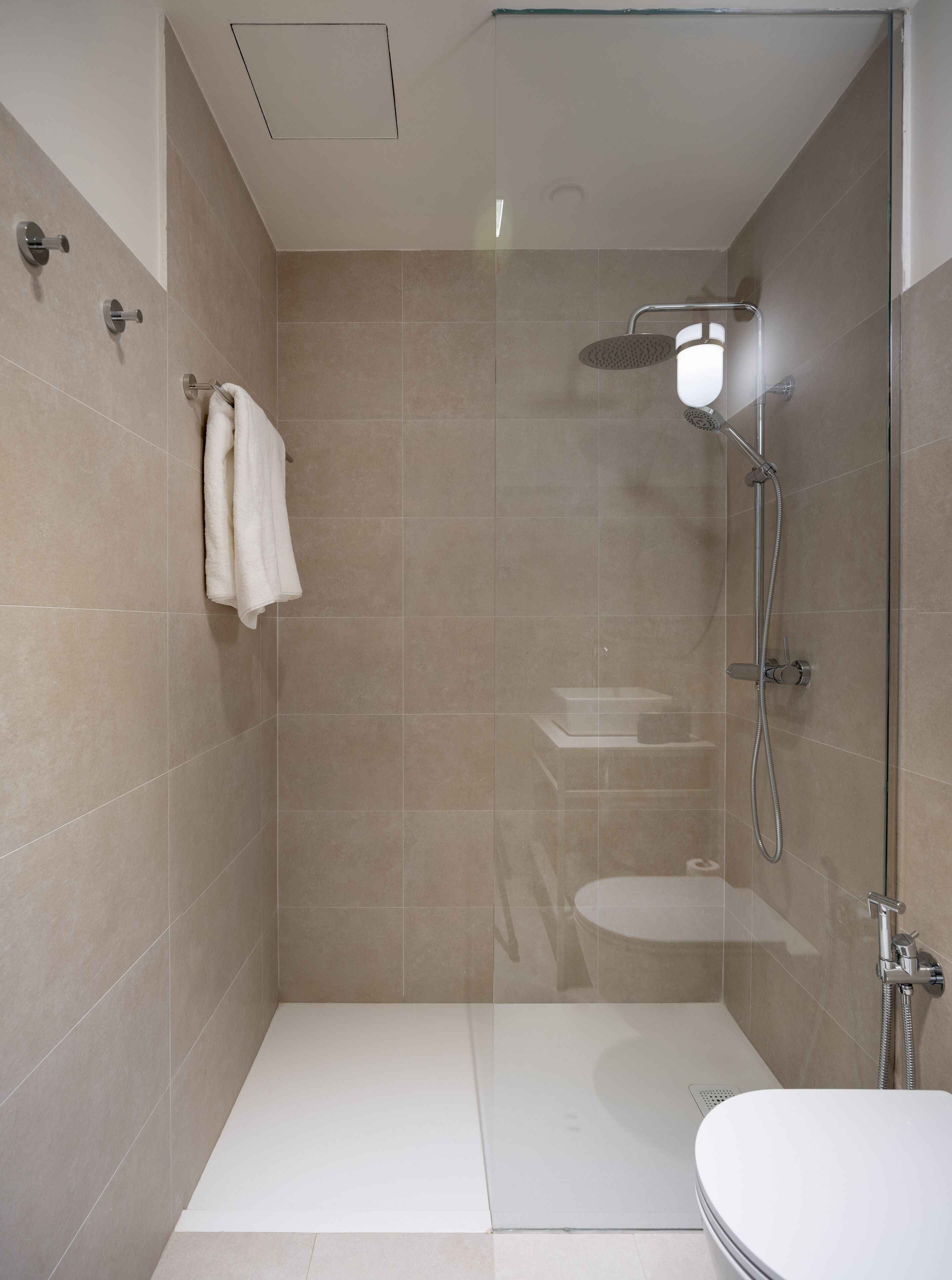 A modern shower area with a glass door, a white bathtub, and a towel rack.