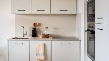 A modern kitchen with white cabinets, a stainless steel sink, and a built-in oven.
