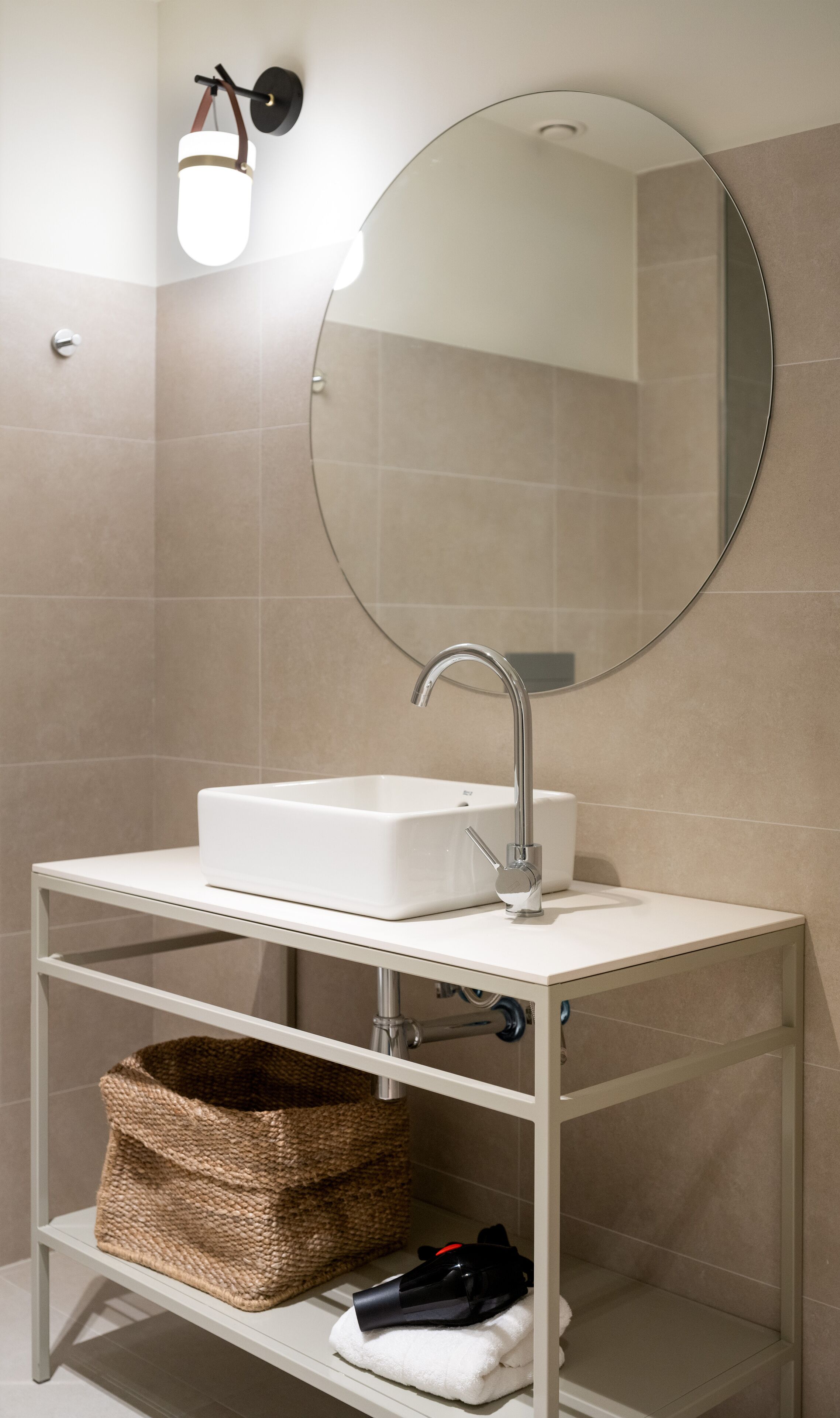A bathroom with a white sink, a round mirror, and a wall-mounted light fixture.