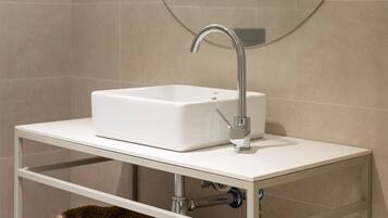 A bathroom with a white sink, a round mirror, and a wall-mounted light fixture.