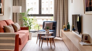 A modern living room with a sofa, armchair, coffee table, and a view of buildings through large windows. - Aparthotel Libere Vitoria (Vitoria-Gasteiz)