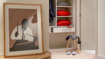 Een kamer met een ingelijste afbeelding, een wit wandrek met rode kussens, en een klein krukje met een gestreept doek.