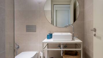Une salle de bain moderne équipée de toilettes, d’un lavabo et d’une douche. Un miroir est placé au-dessus du lavabo et un porte-serviettes en dessous.