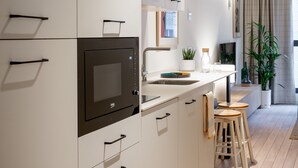 A modern kitchen with white cabinetry, a black microwave, a sink, and wooden stools. - Aparthotel Libere Vitoria (Vitoria-Gasteiz)
