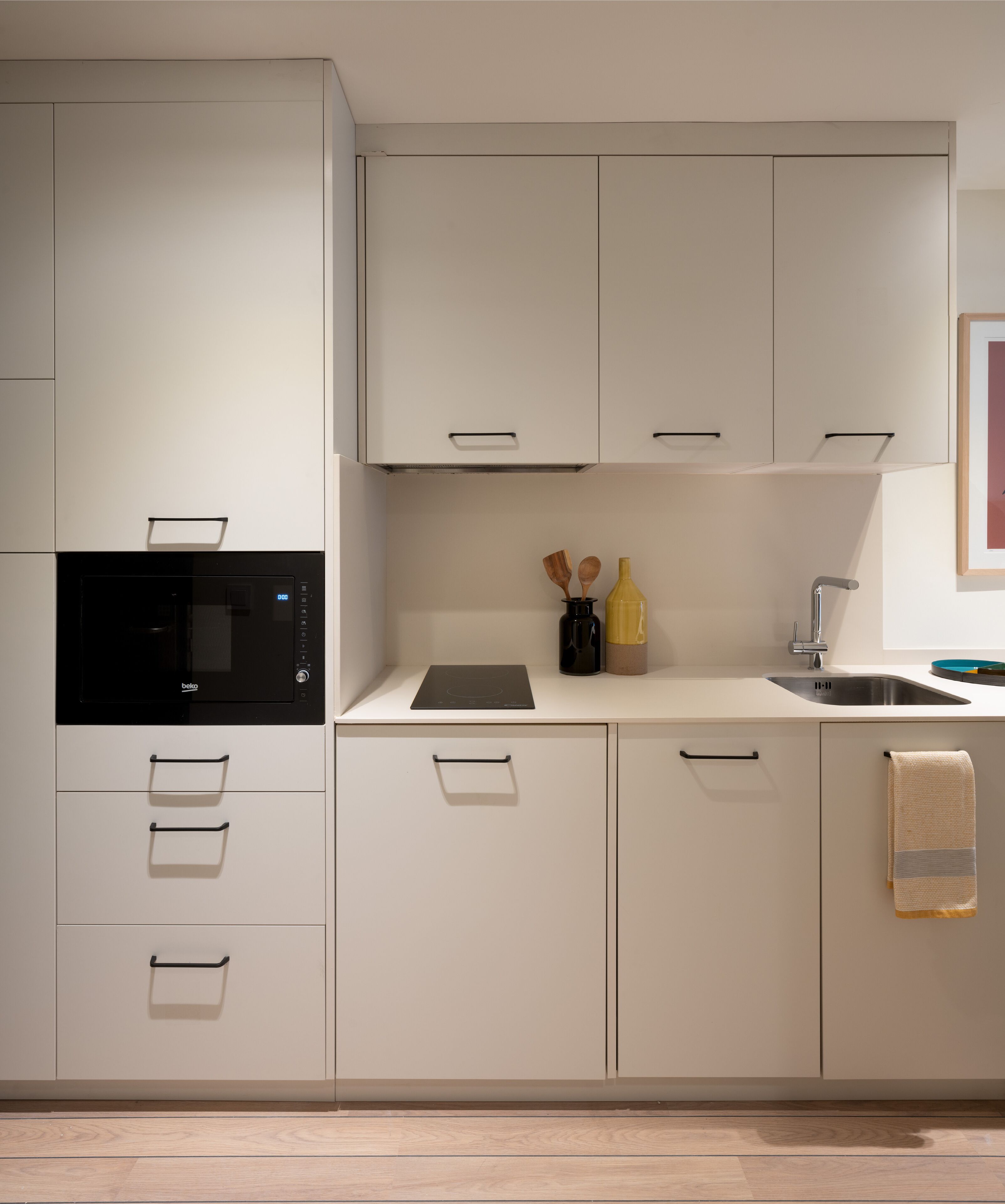 A modern kitchen with white cabinetry, a built-in microwave, a sink, and a countertop with a bottle and wooden utensils.