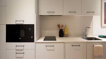 A modern kitchen with white cabinetry, a built-in microwave, a sink, and a countertop with a bottle and wooden utensils.