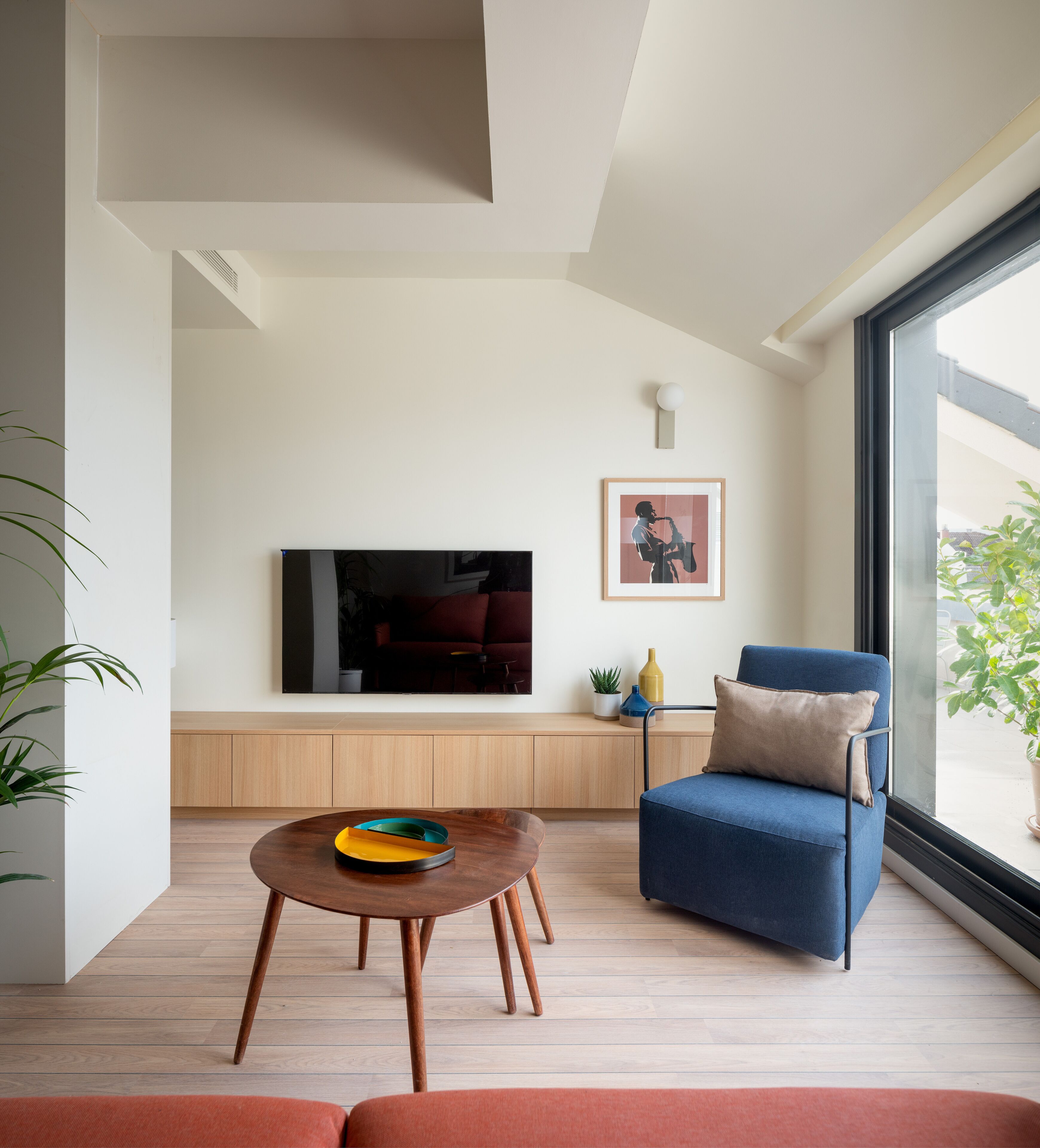 A modern living room with a large TV, a blue armchair, a wooden coffee table, and a view of the outdoors.