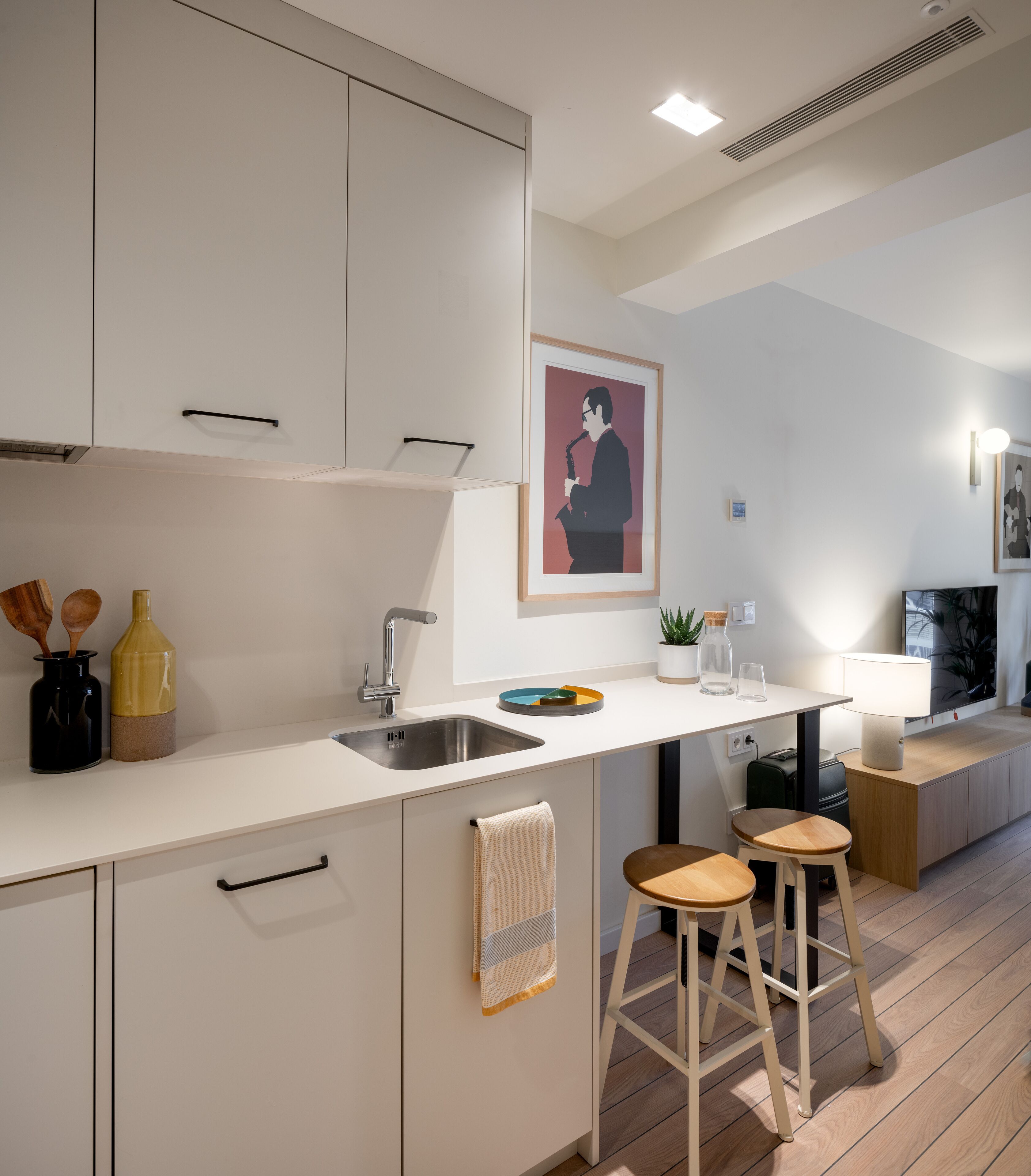 Een moderne keuken met witte kastjes, een roestvrijstalen spoelbak en houten krukken.