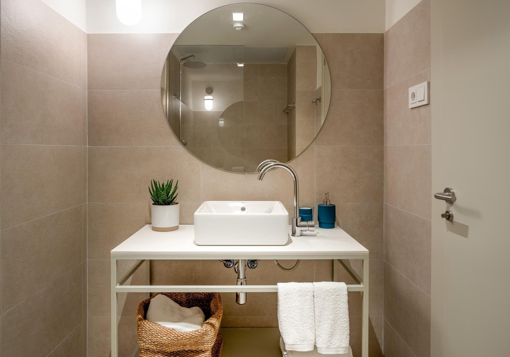 A bathroom with a round mirror, white sink, and a potted plant.