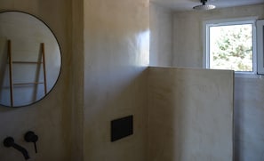 Une salle de bain dotée d’un grand miroir, d’un porte-serviettes, d’une zone de douche et d’une fenêtre donnant sur les arbres.
