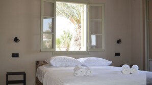 A bedroom with a bed, a ceiling fan, an air conditioning unit, a window, a nightstand, and a chair.