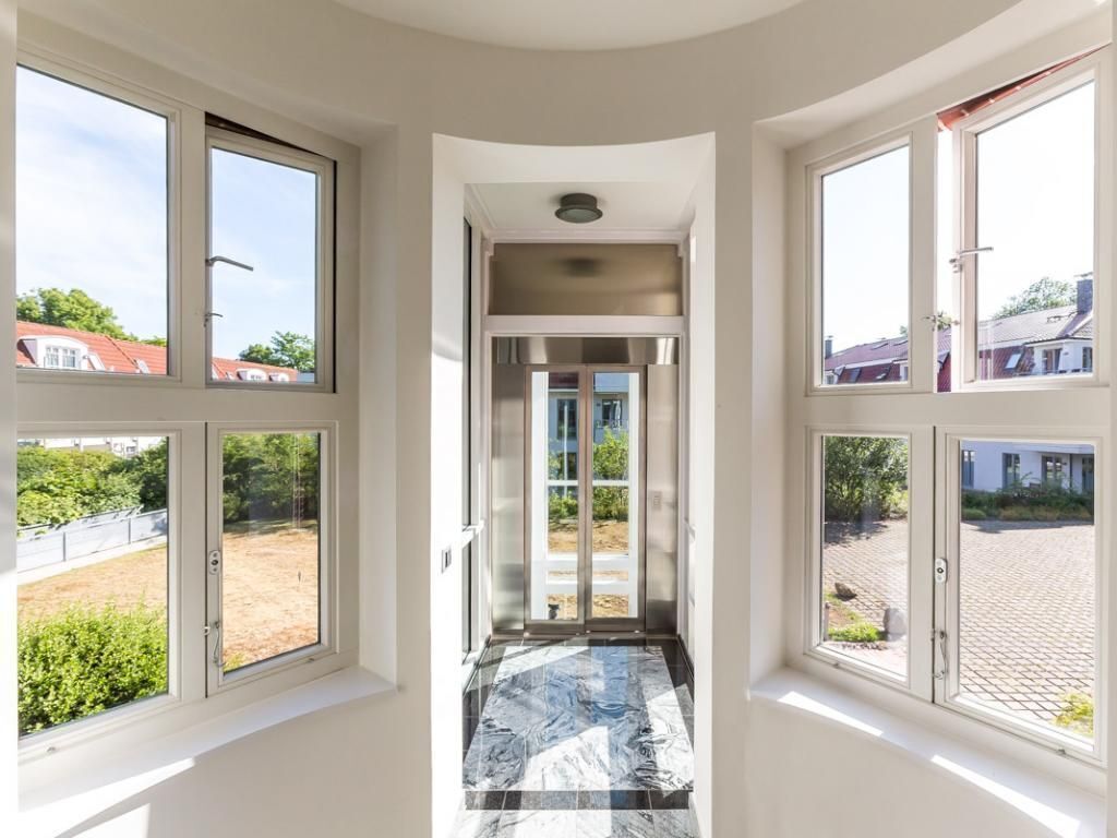 A corridor with large windows on both sides, leading to a door with glass panels.