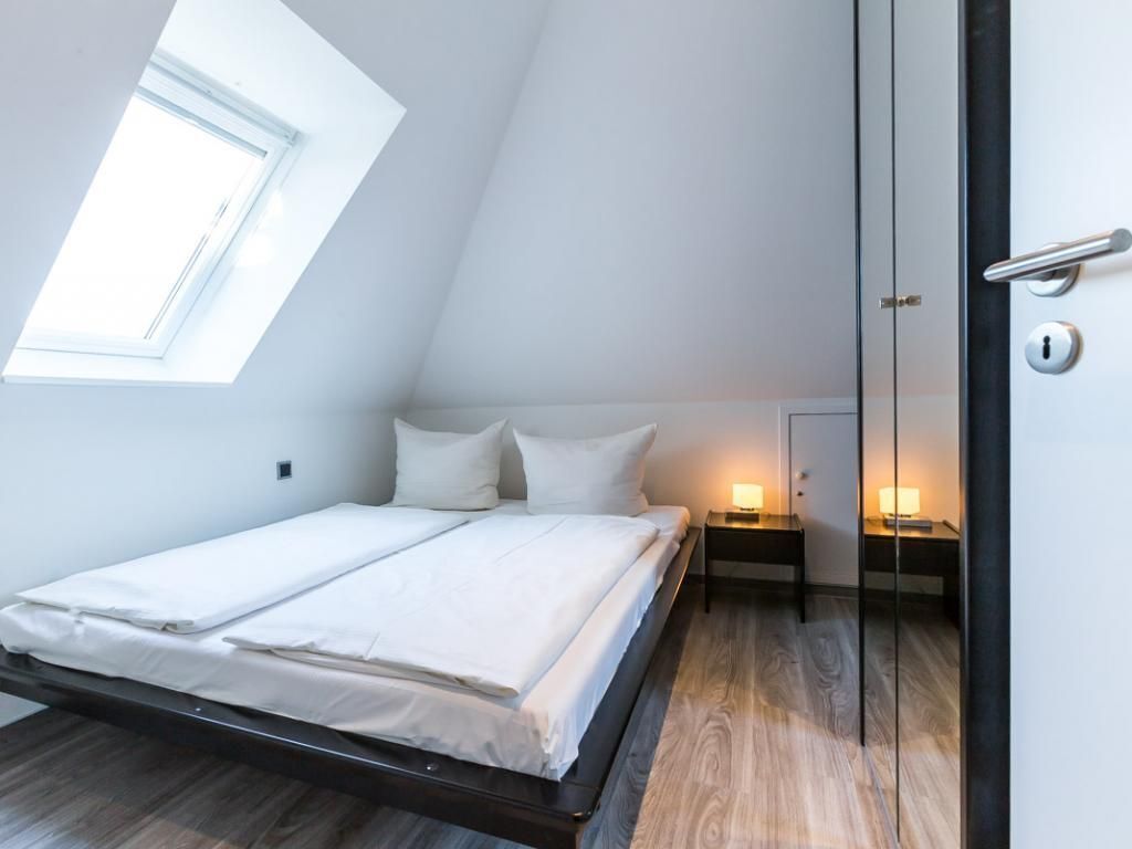 Un dormitorio con cama, mesitas de noche y una ventana.