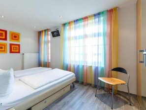 A room with a bed, a chair, and a window with colorful curtains.