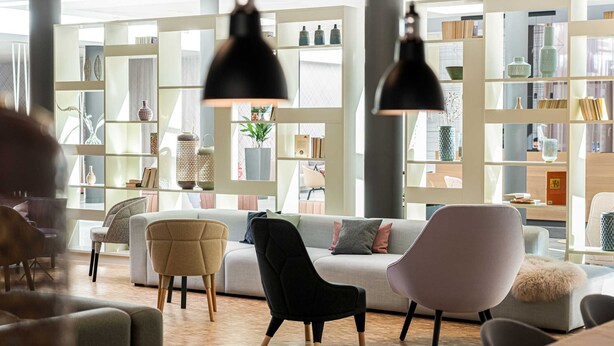A modern living room with a sofa, chairs, and a bookshelf filled with decorative items. - Juniorsuite Typ B - Saline 1822, Hotel Bad Rappenau (Bad Rappenau)