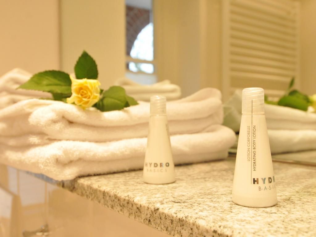 A bathroom with stacked towels, a yellow rose, and two bottles of HYDRO BASICS lotion.