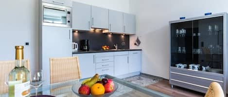 Een moderne keuken met een inbouwoven, een eethoek met een glazen tafel, rieten stoelen en een fruitschaal.