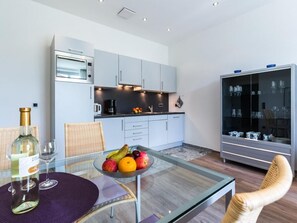 Eine moderne Küche mit Einbauofen, einem Essbereich mit Glastisch, Korbstühlen und einer Obstschale.