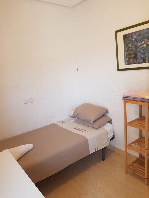 A small, single-bed room with a wooden nightstand and a painting on the wall.
