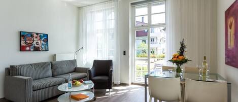 A modern living room with a sofa, armchair, coffee table, and dining table.