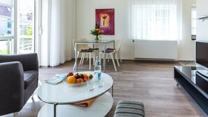 Moderni olohuone, jossa on pyöreä pöytä, sohva, ruokailutila tuoleineen, televisio ja suuri ikkuna, jossa on verhot.