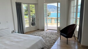 Ein Schlafzimmer mit einem großen Bett, einem Sessel und Meerblick durch offene Türen.