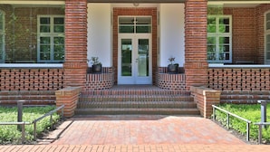 A brick building with a central entrance, two potted plants on either side, and a brick pathway leading to the entrance.