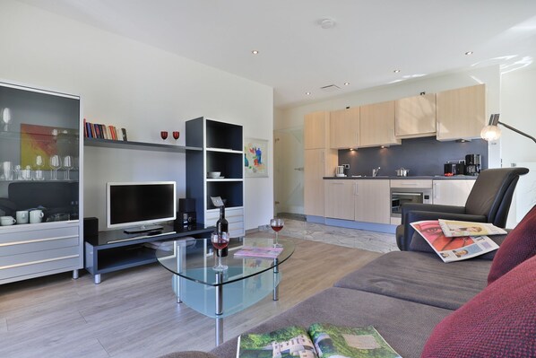 A modern living room with a glass coffee table, a flat-screen TV, and a sofa with magazines.