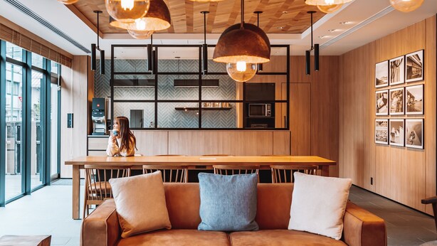 Een modern interieur met een houten plafond, hanglampen, een keukenhoek en een zithoek met een bank en tafel.