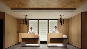 Een moderne hotel receptie met houten lambrisering, twee balies en hanglampen.
