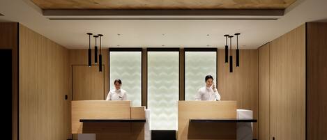 A modern hotel reception area with wooden paneling, two reception desks, and pendant lighting.
